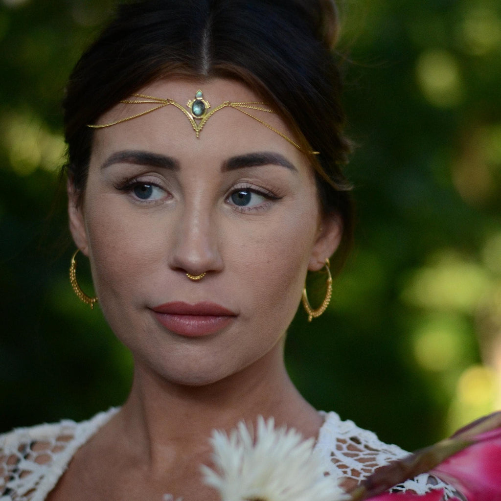 A model wearing a v-shaped gold head chain, with a blue labradorite gemstone and three chains draping on the sides.