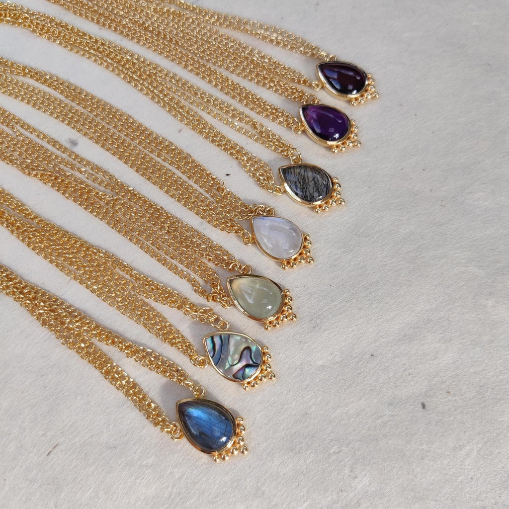 A collection of seven bohemian gold head chains with drop-shaped gemstones, showcasing the different gemstone colors.