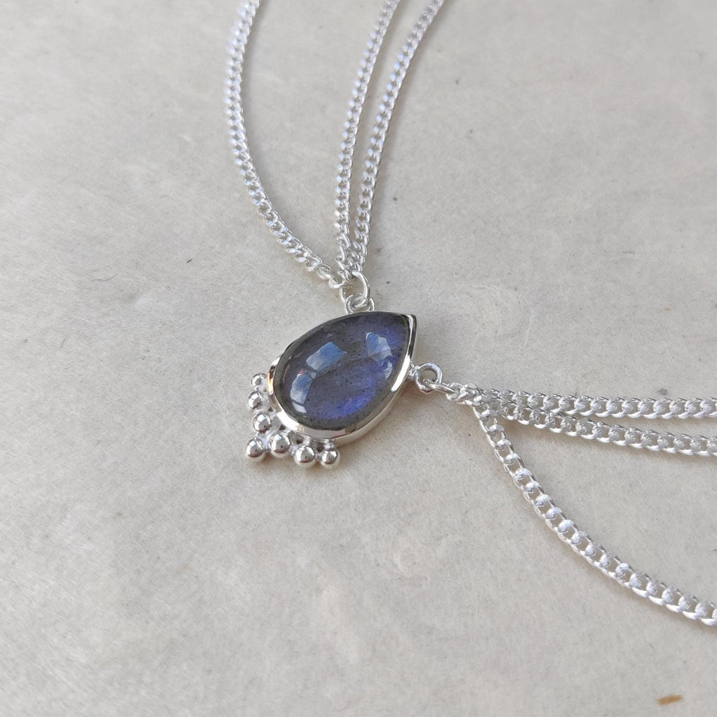 Close-up of a silver head chain with drop-shaped blue labradorite gemstone centerpiece, and three chains draping on each side.