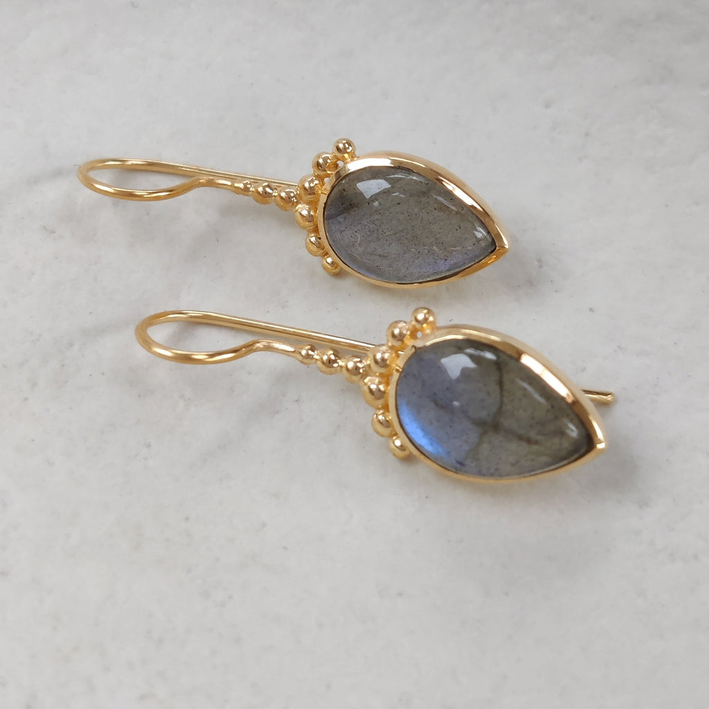 Drop-shaped gold earrings with Labradorite stones on a white dish