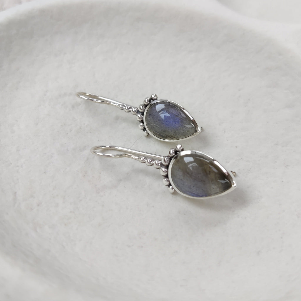 Pair of silver earrings with labradorite gemstones on a white dish.