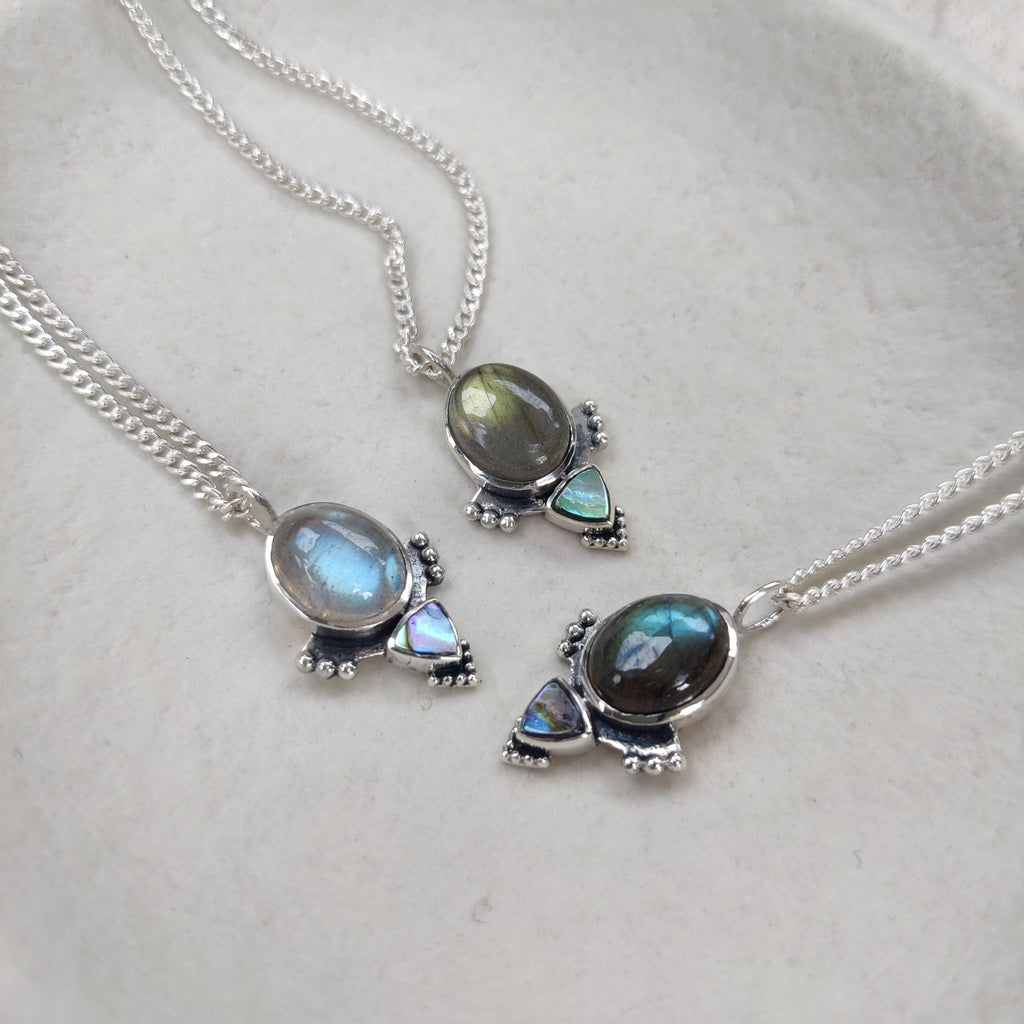 Three silver necklaces with labradorite gemstone pendants on a light background. Displayed side by side to show the natural blue and green colors of labradorite.