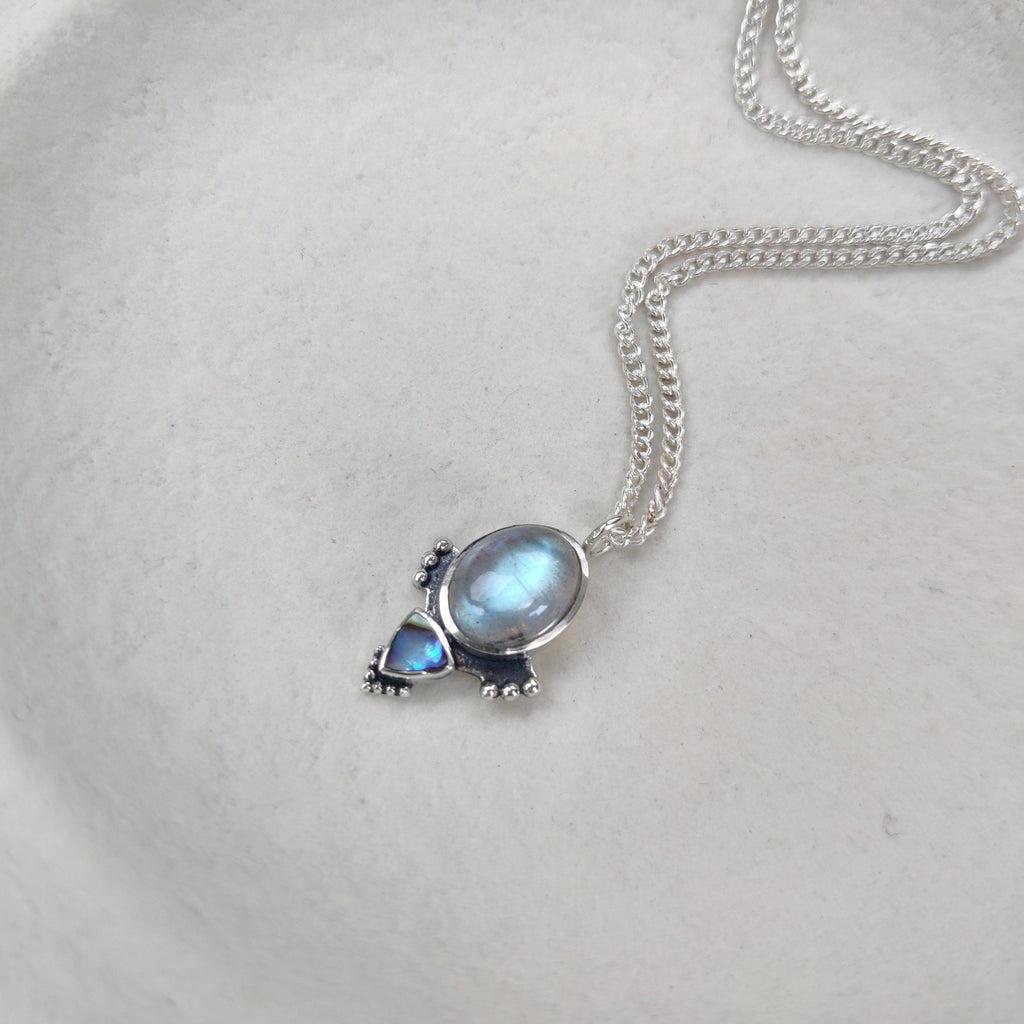 Silver necklace with a pendant featuring blue labradorite gemstones on a white surface.