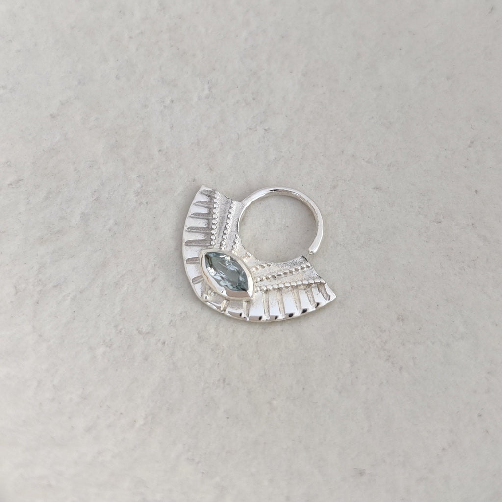 Silver septum nose ring with a blue topaz gemstone on a textured surface