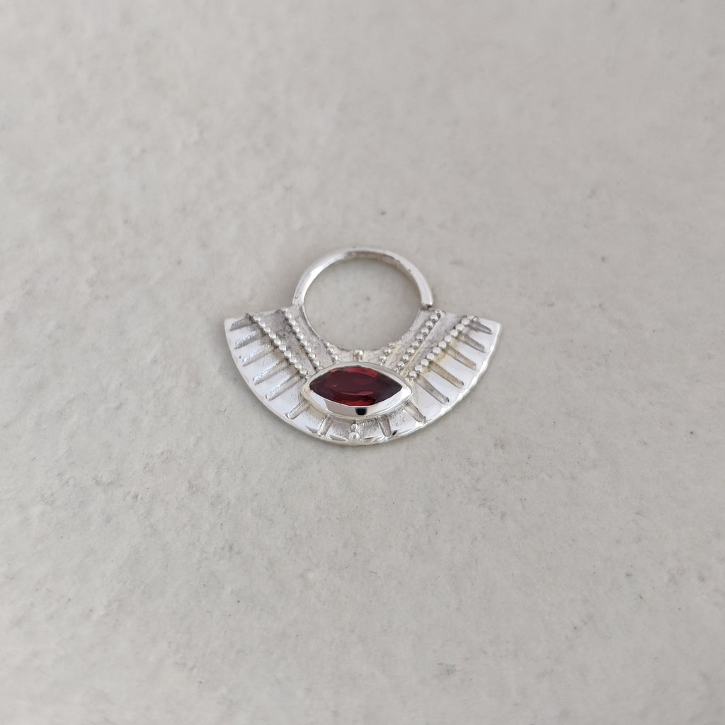Large silver septum with a red gemstone on a textured white surface