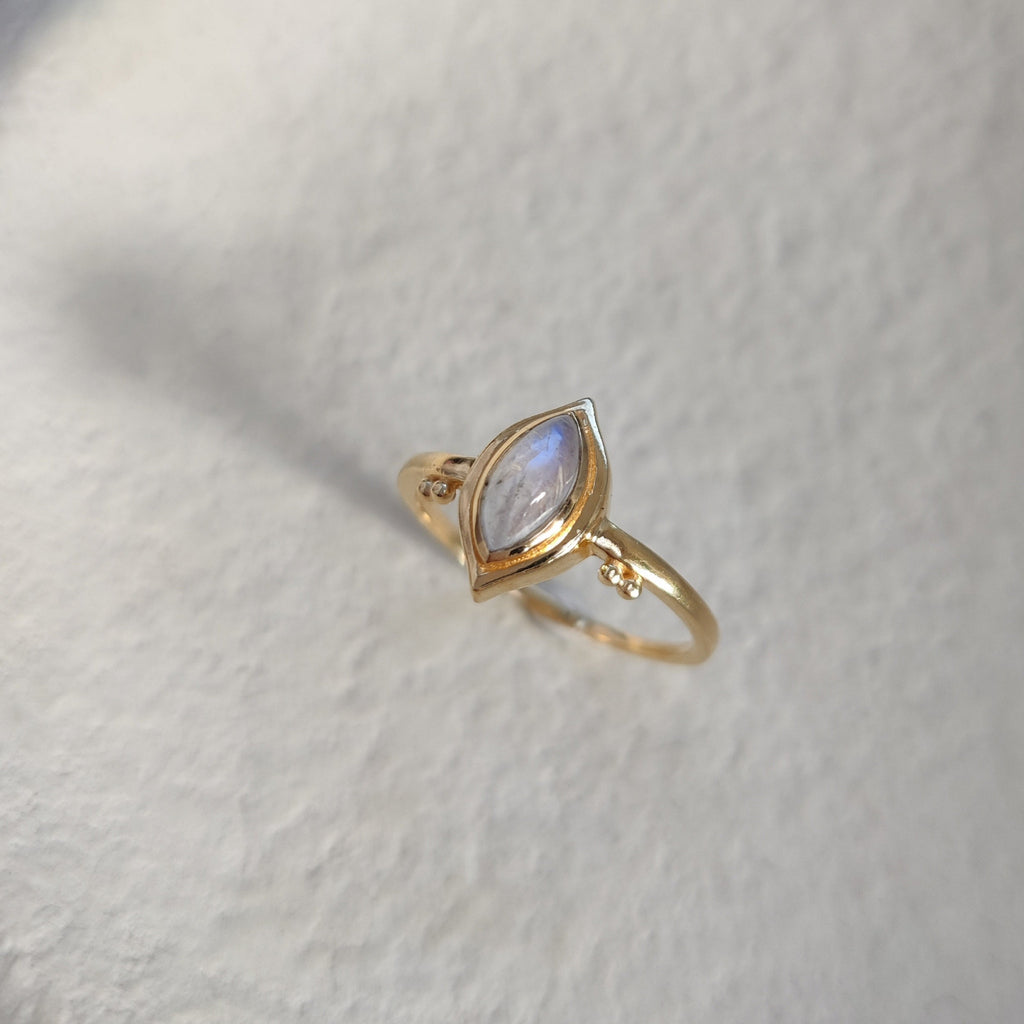Gold ring with a marquise-shaped moonstone on a textured white surface.