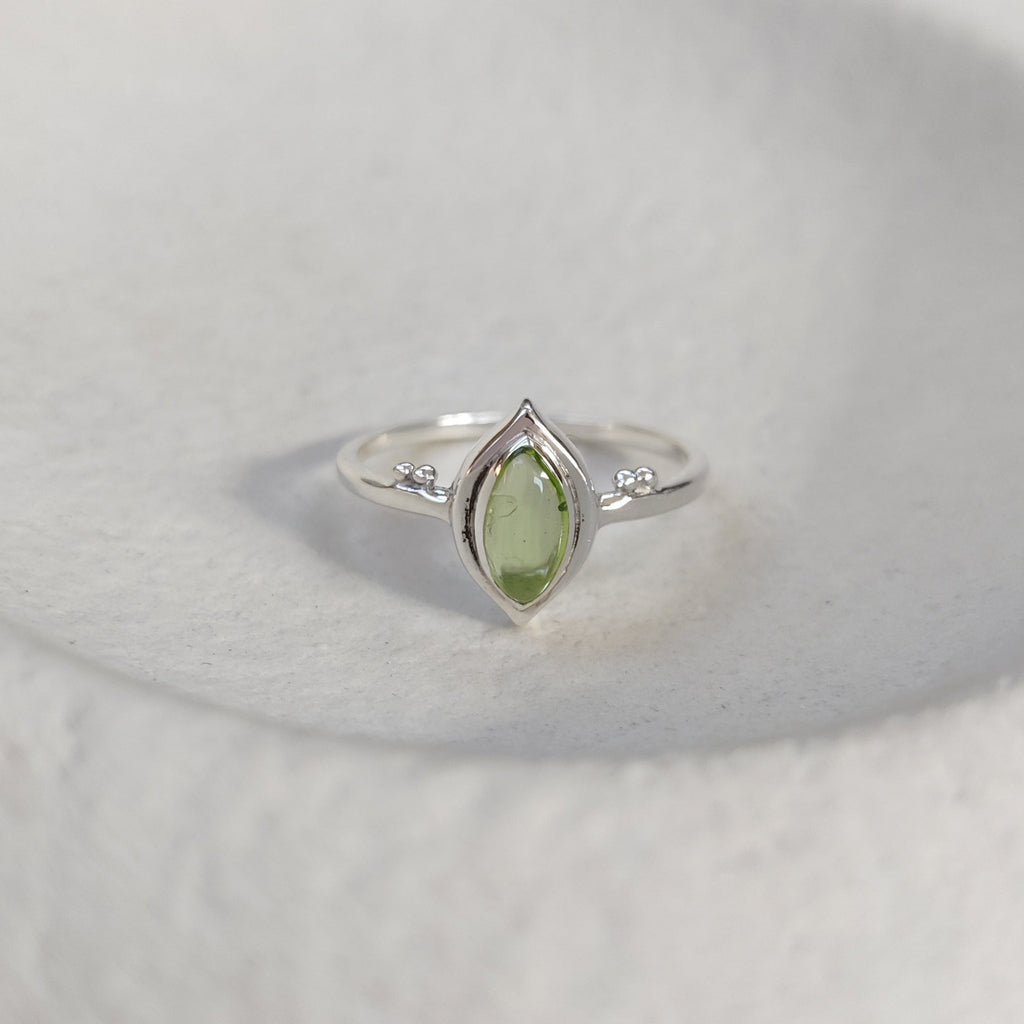 Silver ring with a green gemstone on a textured white surface