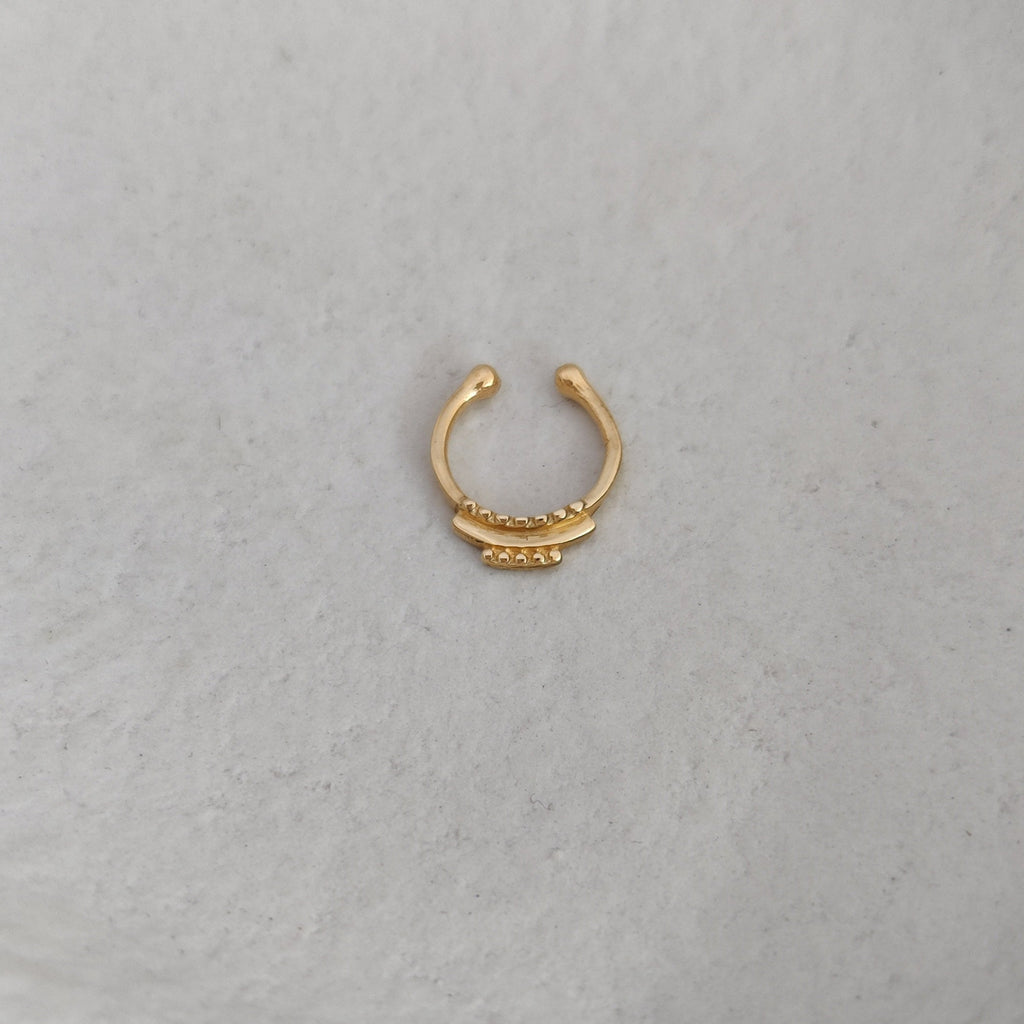 Gold fake septum nose ring on a textured white surface