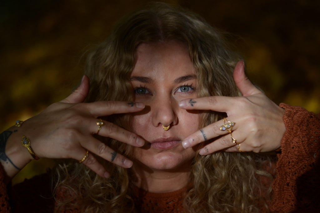 Woman with multiple gold rings on her fingers in a dimly lit setting.