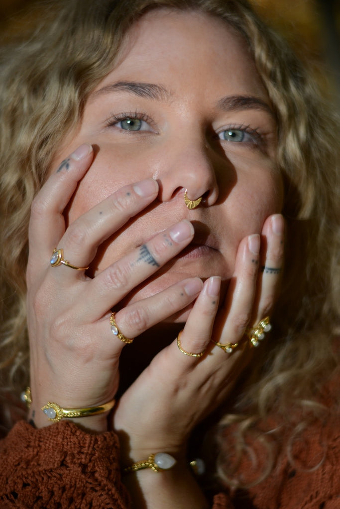 Close-up of a person with multiple gold rings and a nose ring, wearing a brown textured garment.