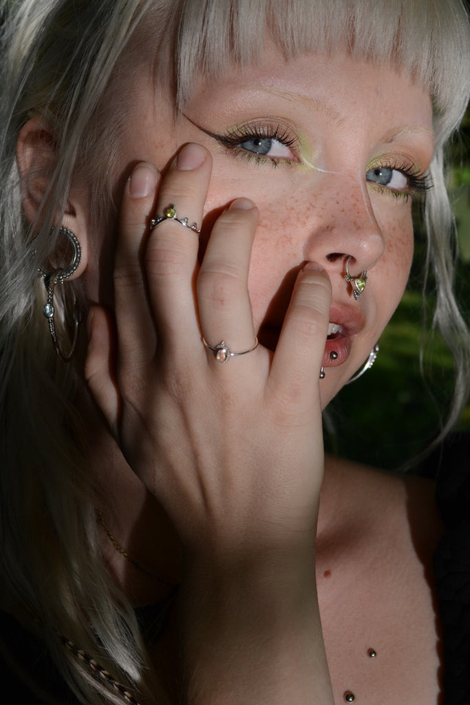 Model wearing multiple silver rings and septum nose rings with green gemstones