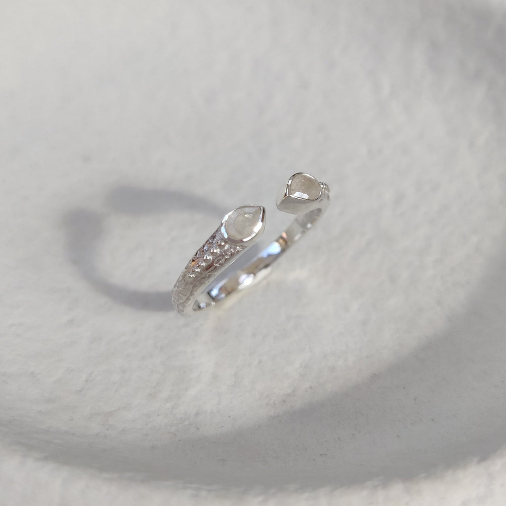 Open cuff silver ring with a small moonstones on a white textured surface