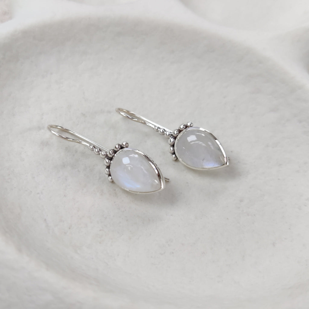 Teardrop-shaped earrings with a light-colored gemstone on a white dish.