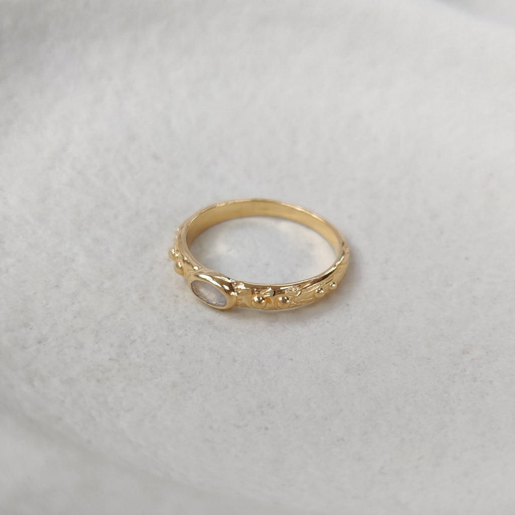 Gold ring with moonstone on a textured white surface