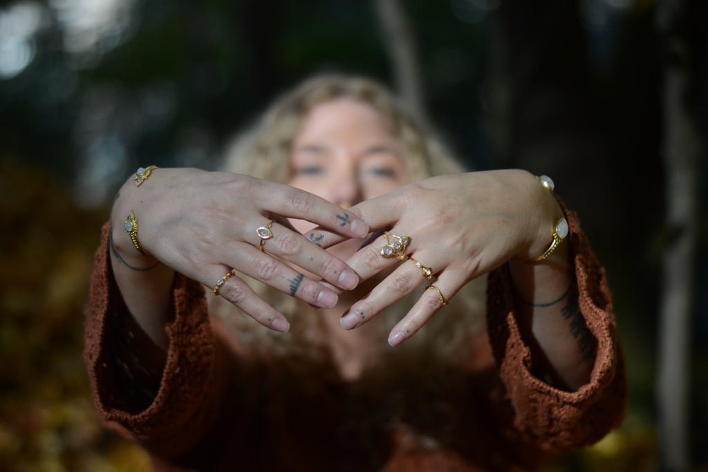 Person wearing multiple gold rings with moonstone on hands with a blurred natural background