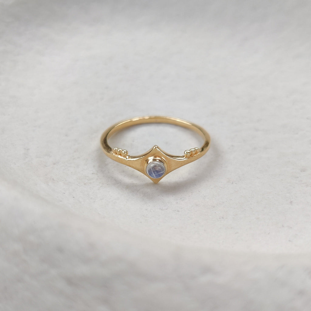 Gold ring with a moonstone on a textured white surface.