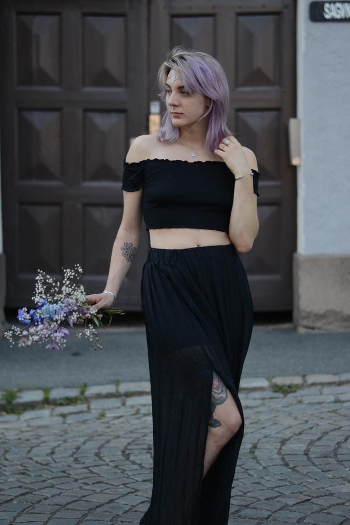 Woman in a black outfit and moonstone head chain holding flowers on a cobblestone street.