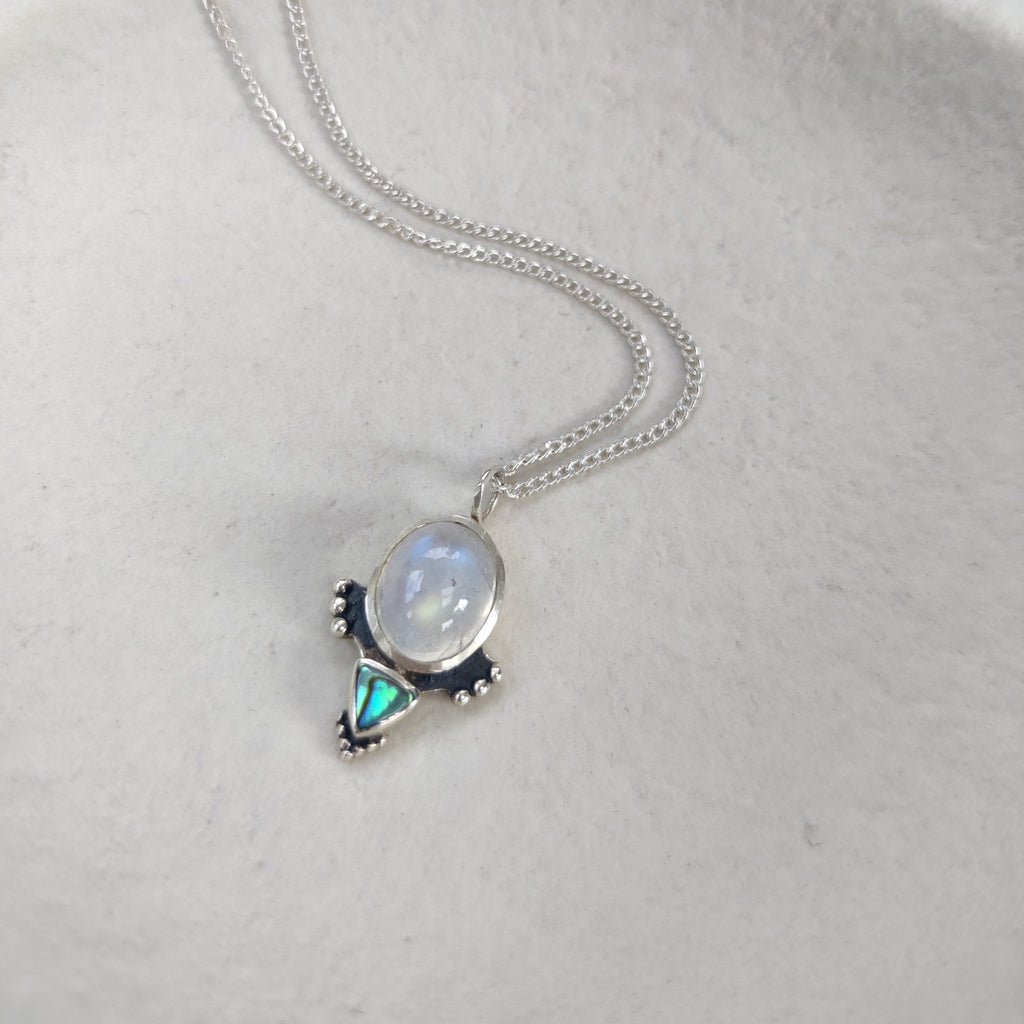 Silver necklace with a pendant featuring a moonstone and a trillion shaped abalone shell.