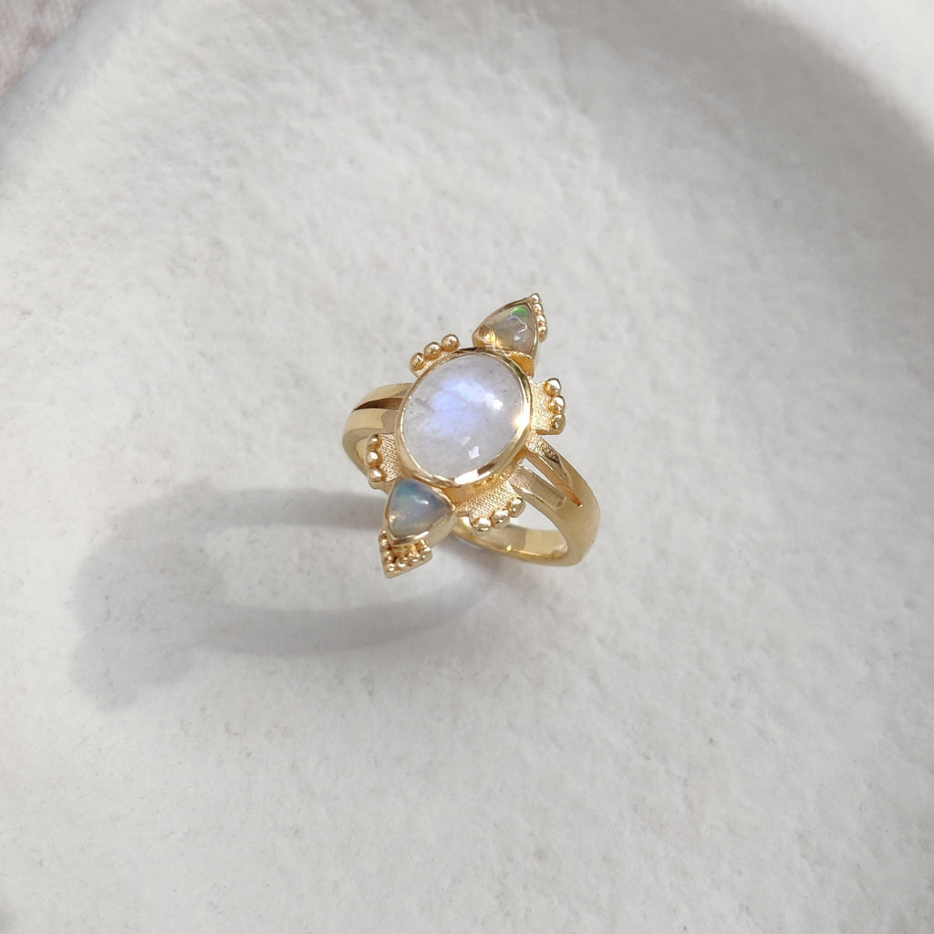 Gold ring with moonstone and opals on a white surface.