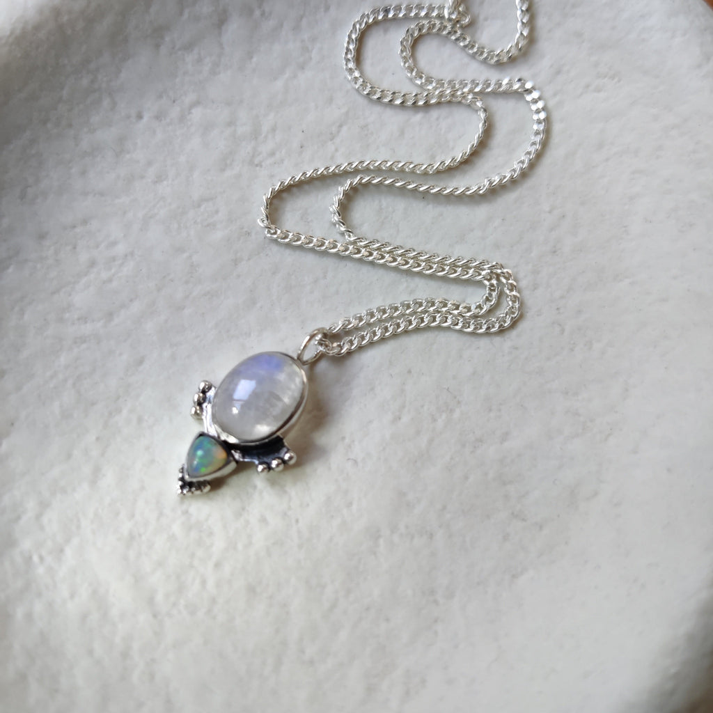A silver necklace with moonstone and opal displayed on a jewelry plate.