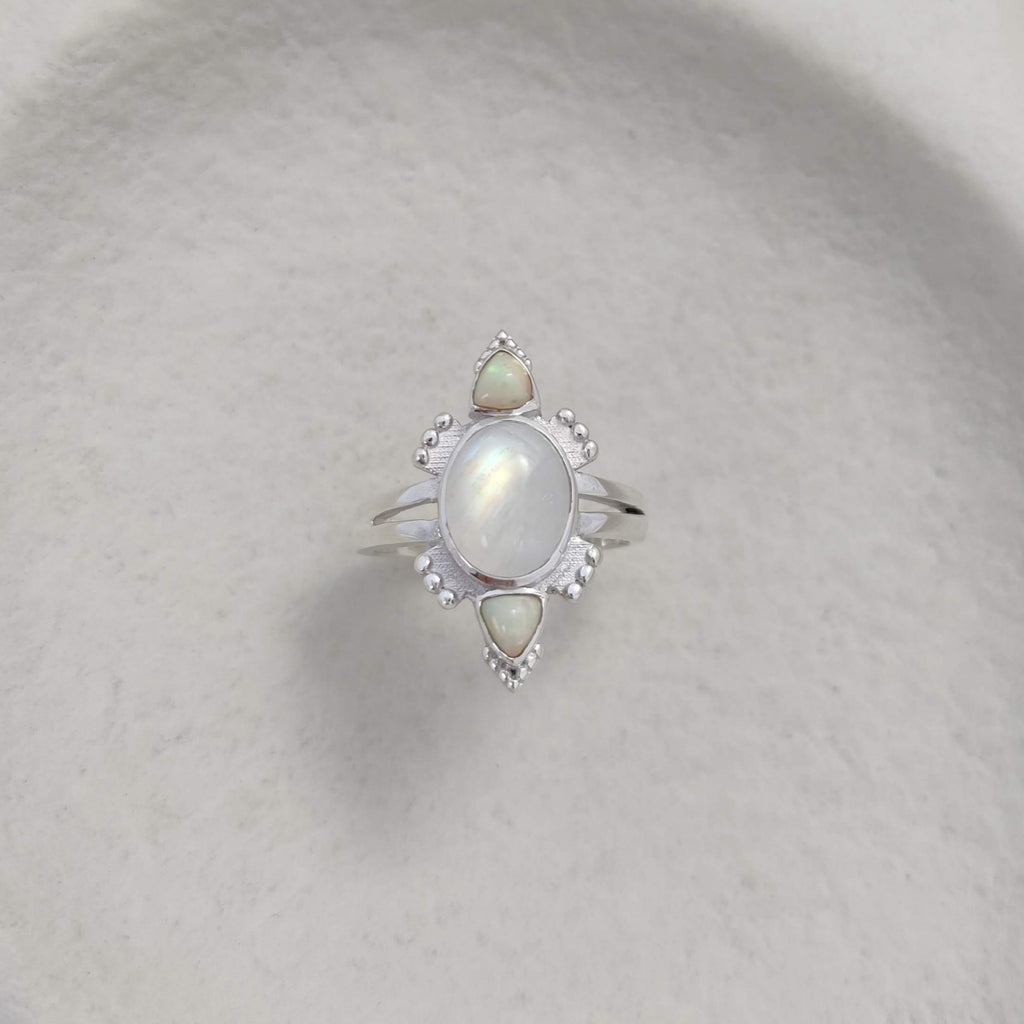 Silver ring with a central moonstone and smaller opal gemstones on a textured surface.