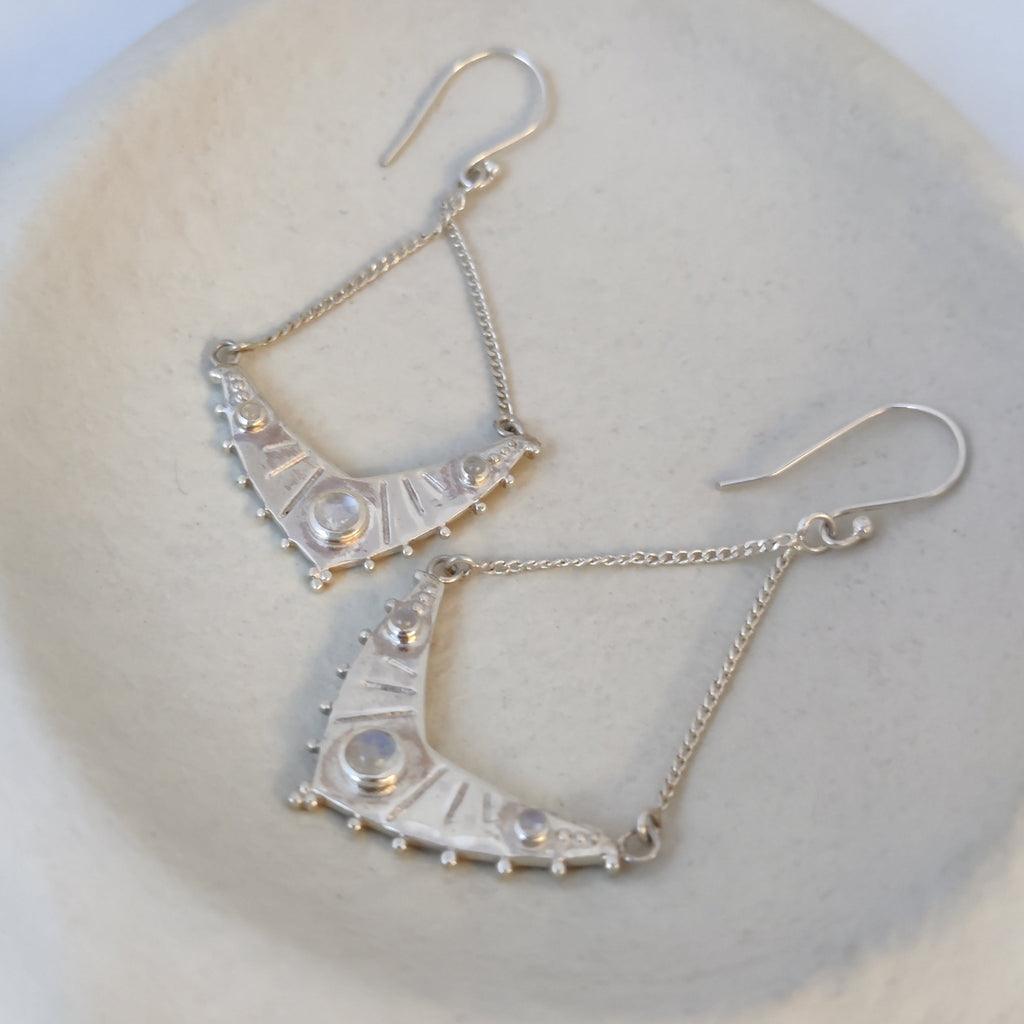 Dangling silver earrings with moonstone, displayed on a jewelry plate.