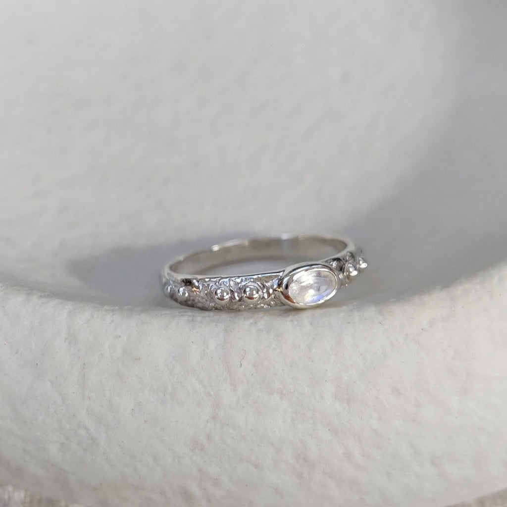 Silver ring with a moonstone on a textured white surface.