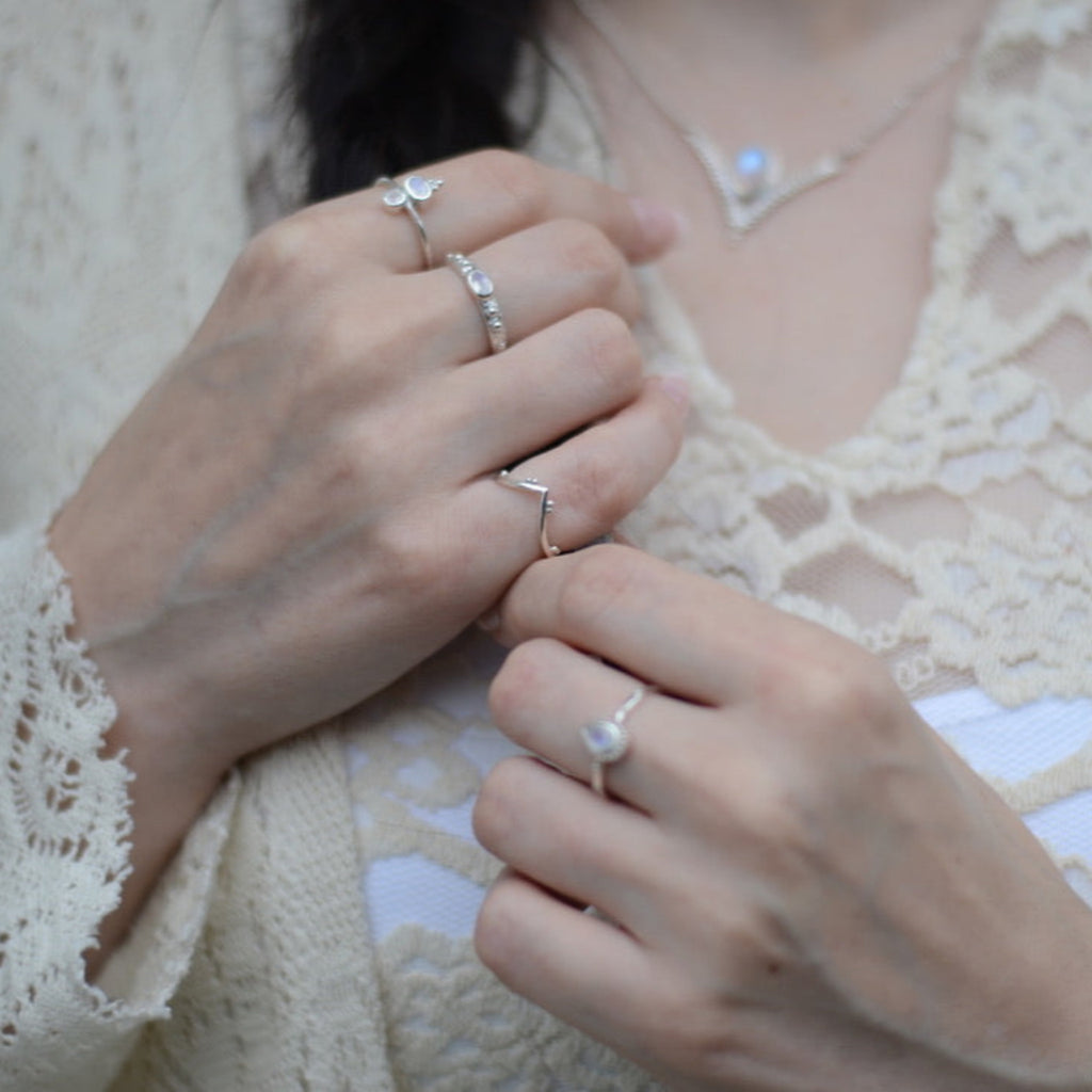 Close-up of hands wearing multiple silver rings on a light background.