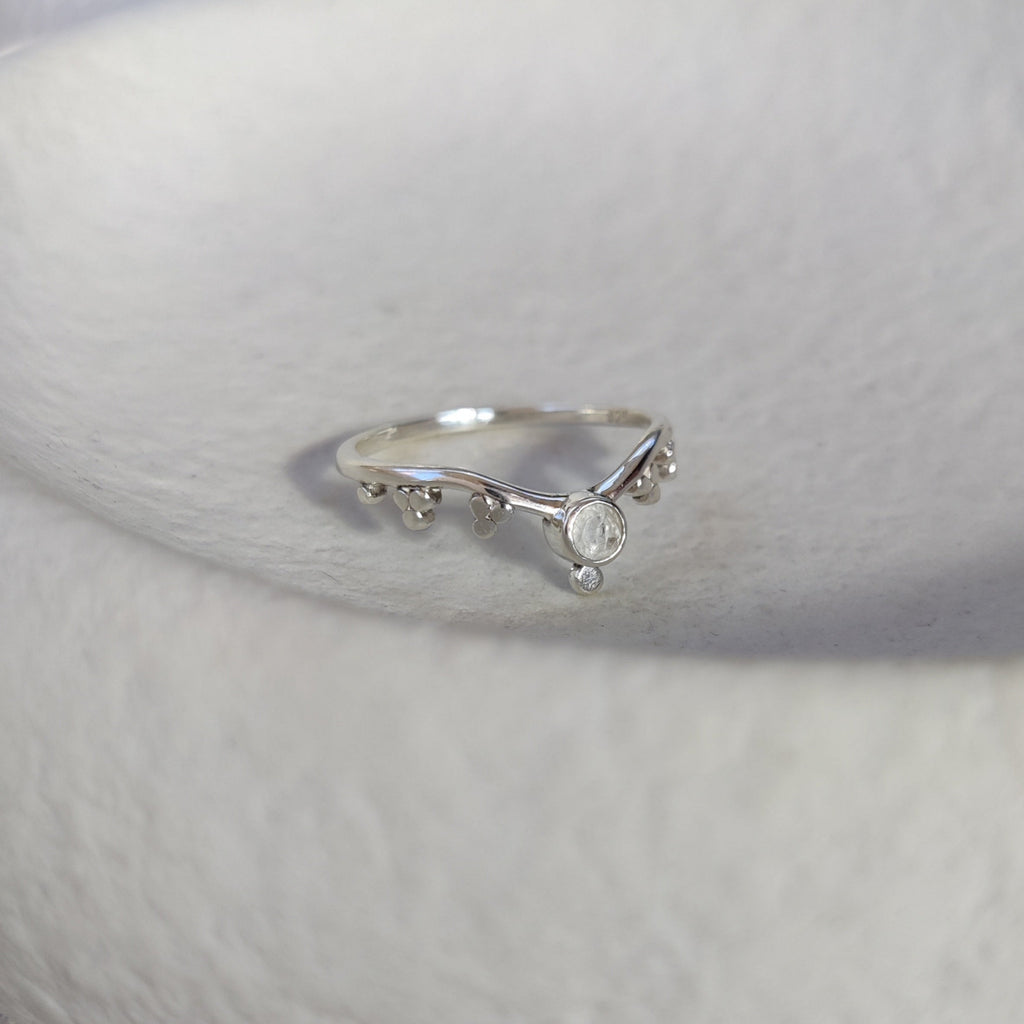 Silver ring with a small moonstone on a textured white surface.