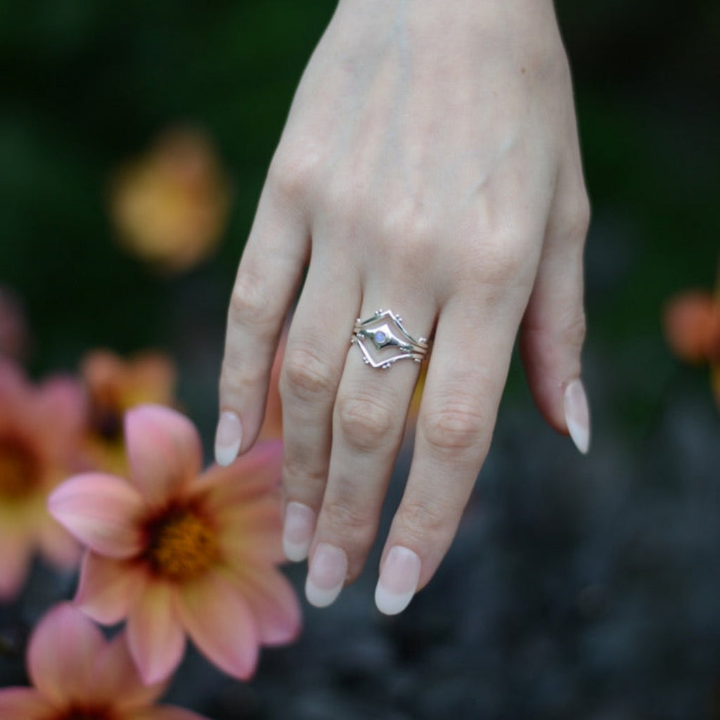 Hand wearing a silver stacking rings with flowers in the background.