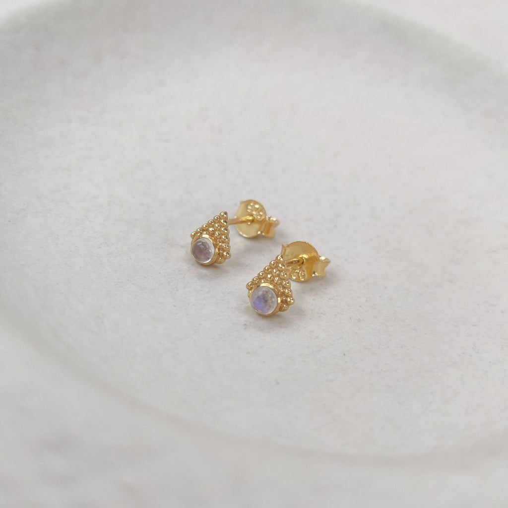 Gold earrings with moonstones on a white plate.