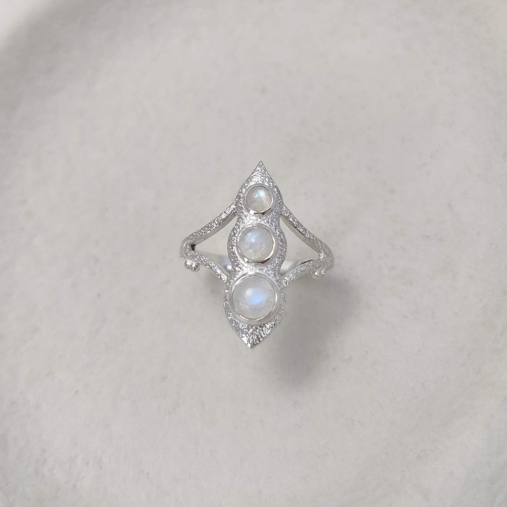 Large silver ring with three gemstones on a white background.