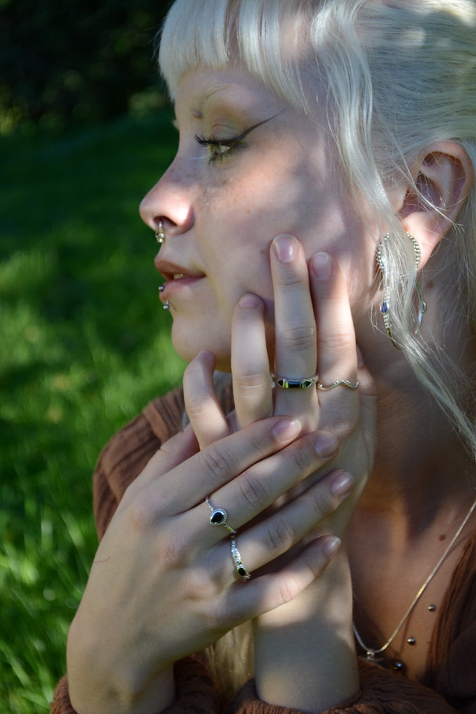 Woman with blonde hair and multiple rings on her finger, outdoors with greenery.