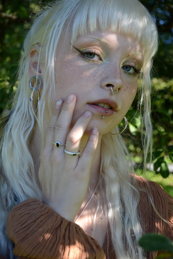Person with blonde hair and silver piercings and rings outdoors