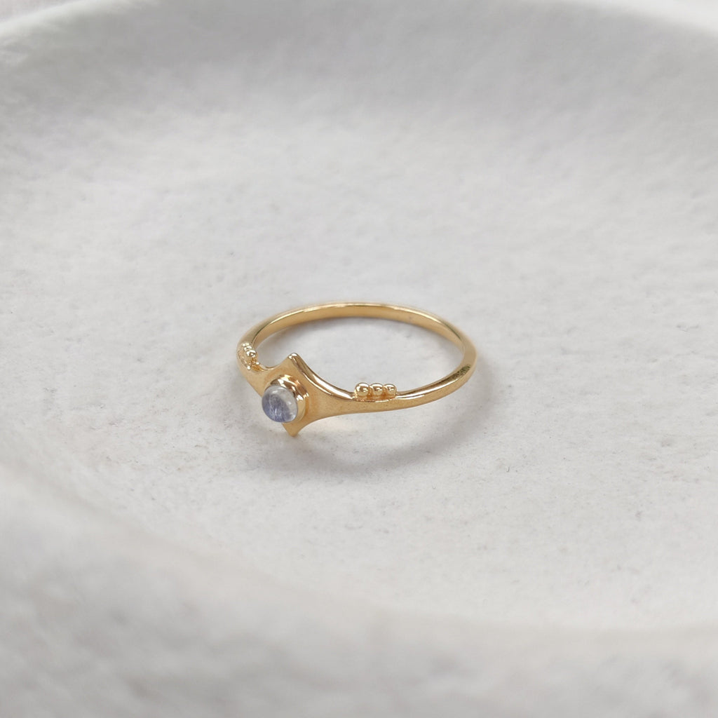 Gold ring with a gemstone on a textured white surface.