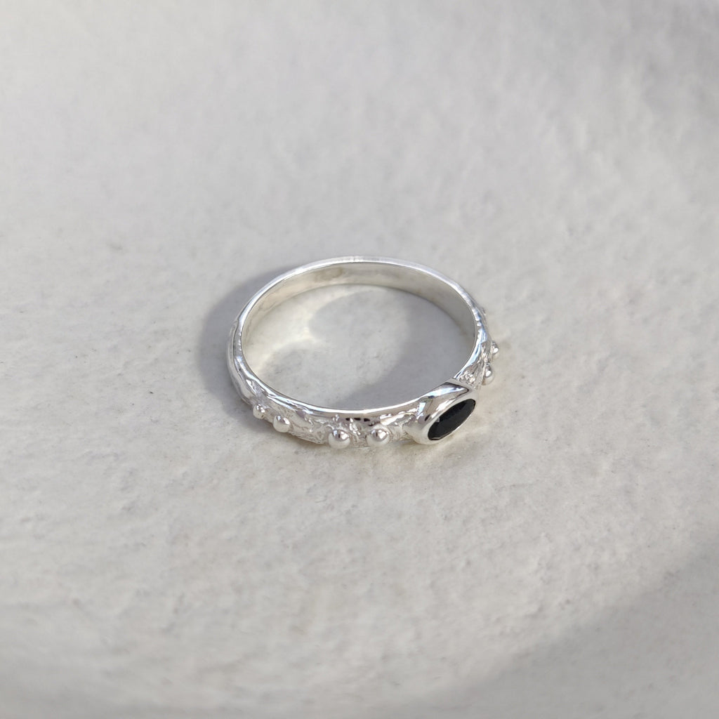 Textured silver ring with a small black gemstone on a light background.