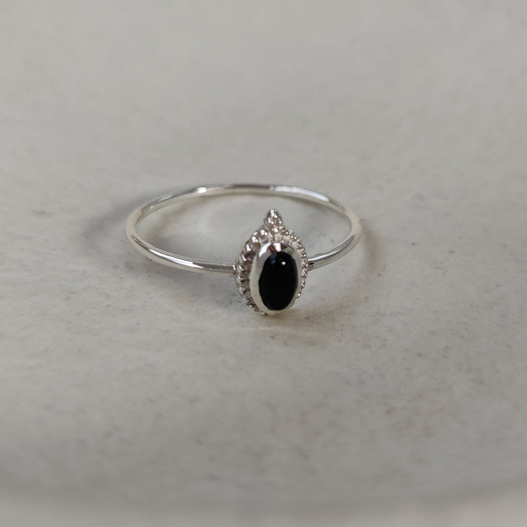 Silver ring with a black gemstone on a light stone surface