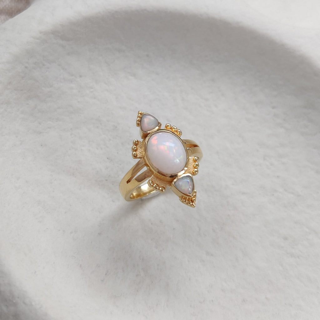 Gold ring with three sparkling opal gemstones on a white dish.