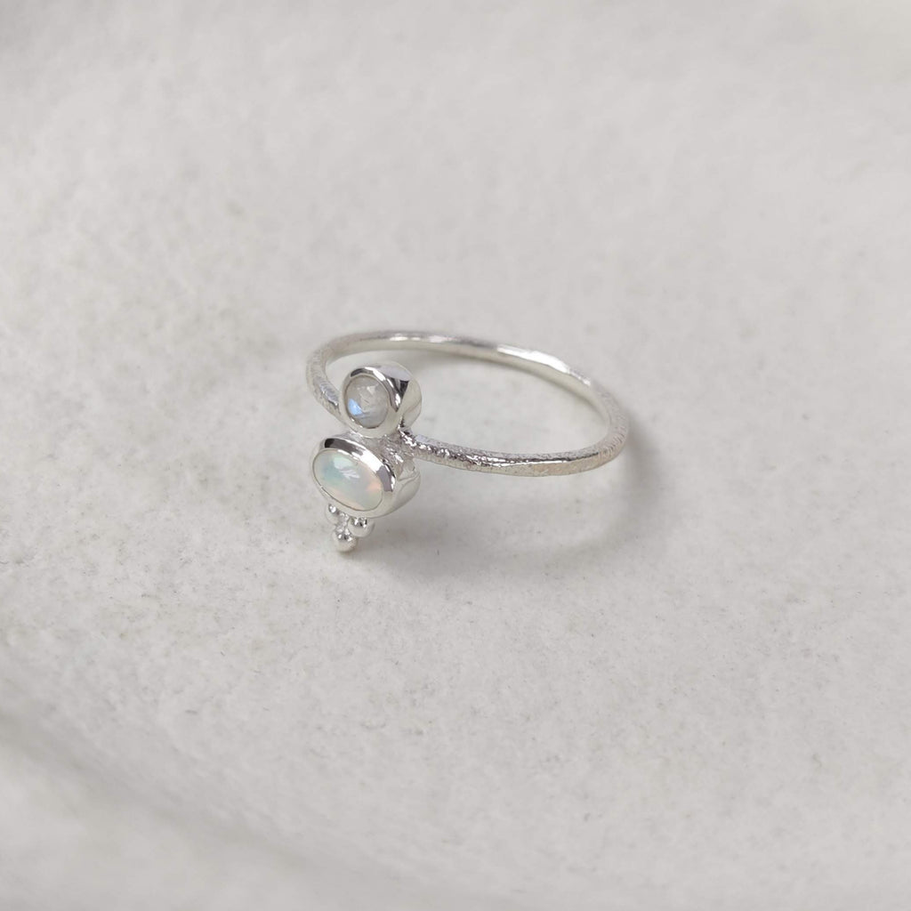 Silver ring with a small opal and moonstone on a white surface.