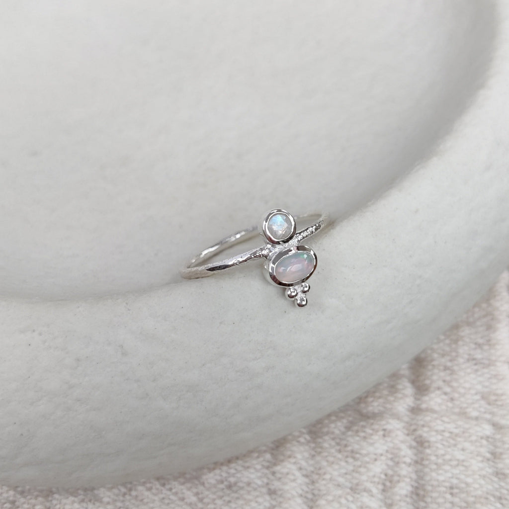 Silver ring with a opal and moonstone on a textured surface.