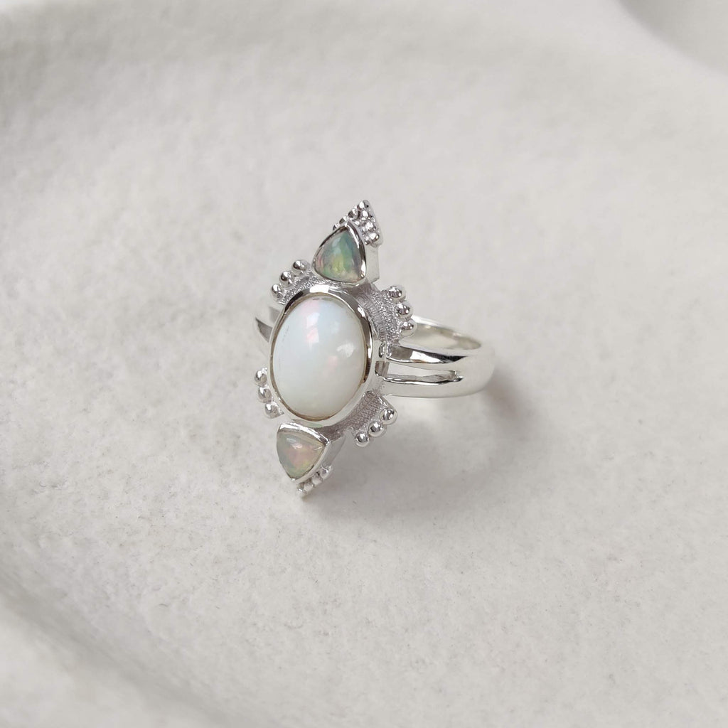 Silver ring with a central opal and smaller opal gemstones on a white surface
