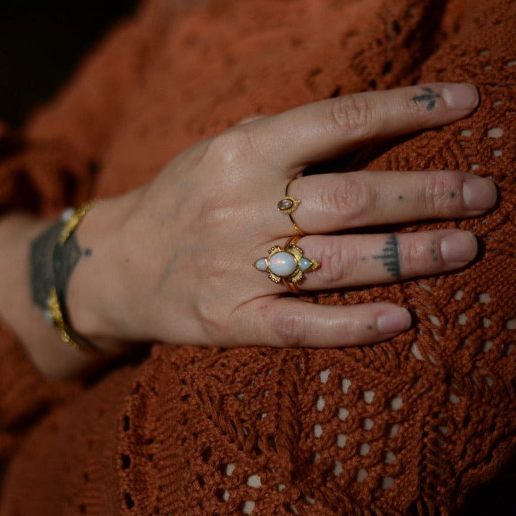 Close-up of a hand with gold rings with opal on a textured brown fabric background