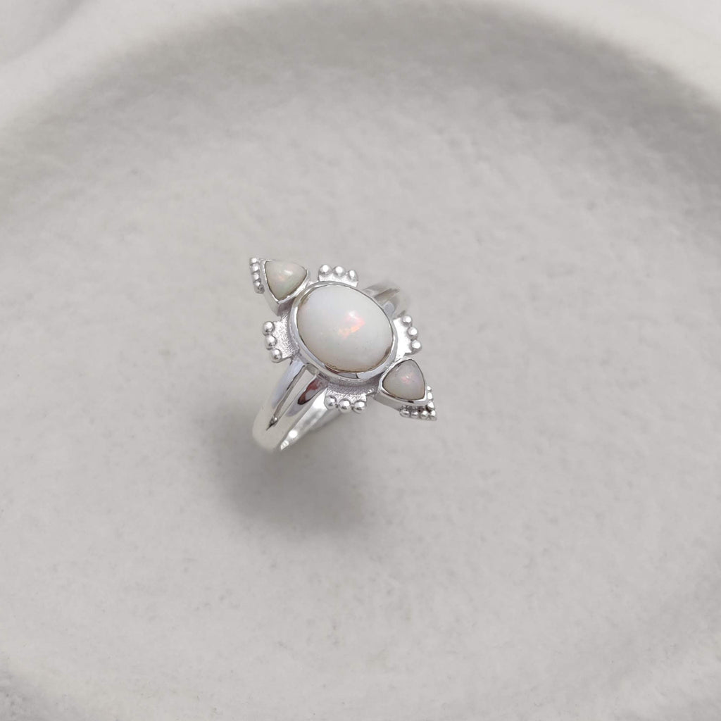 Silver ring with three opal gemstones on a white ceramic dish