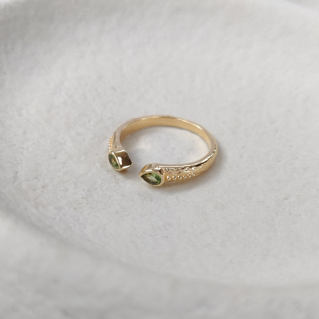 Open cuff gold ring with two green gemstones on a white surface.