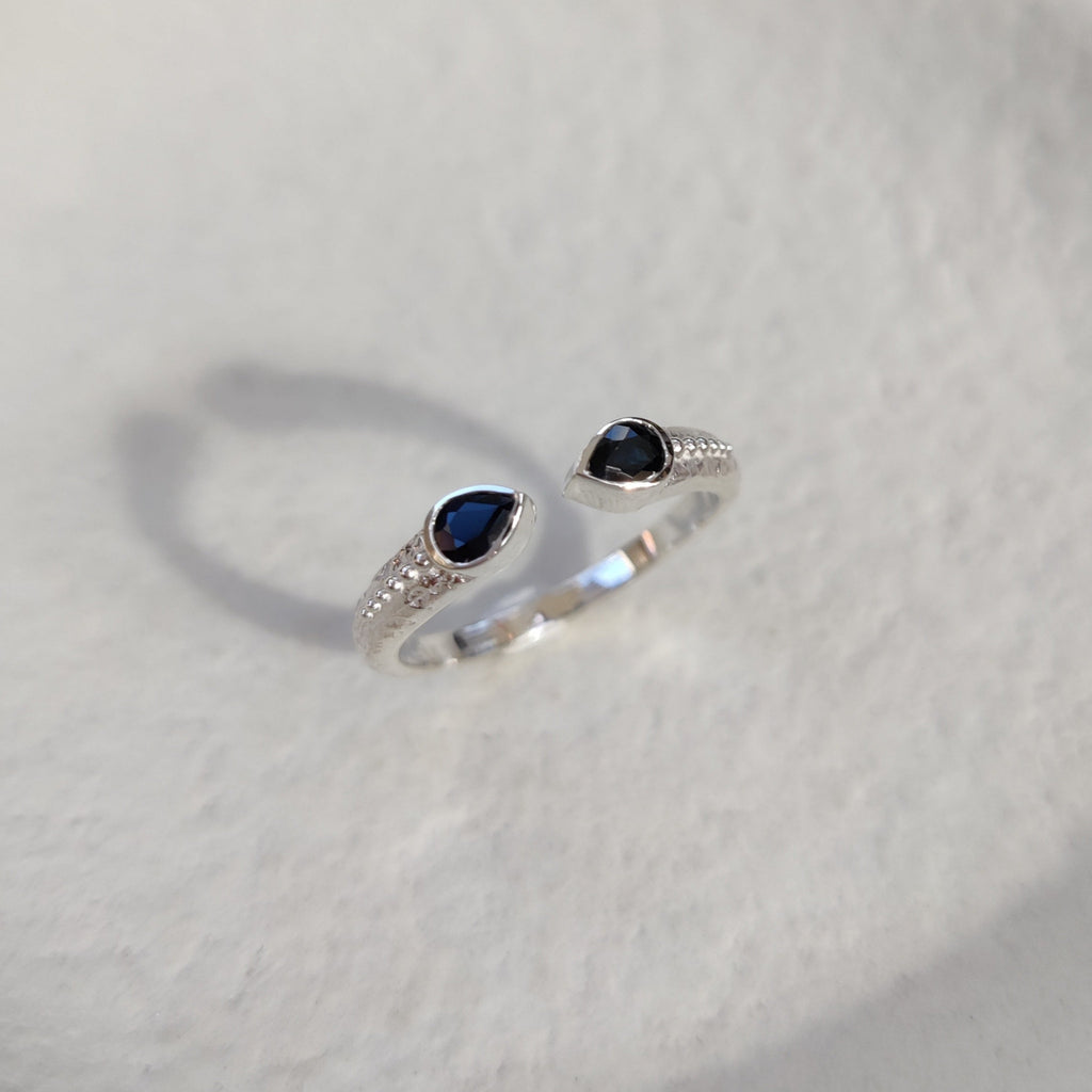 Open cuff silver ring with two gemstones on a textured white surface