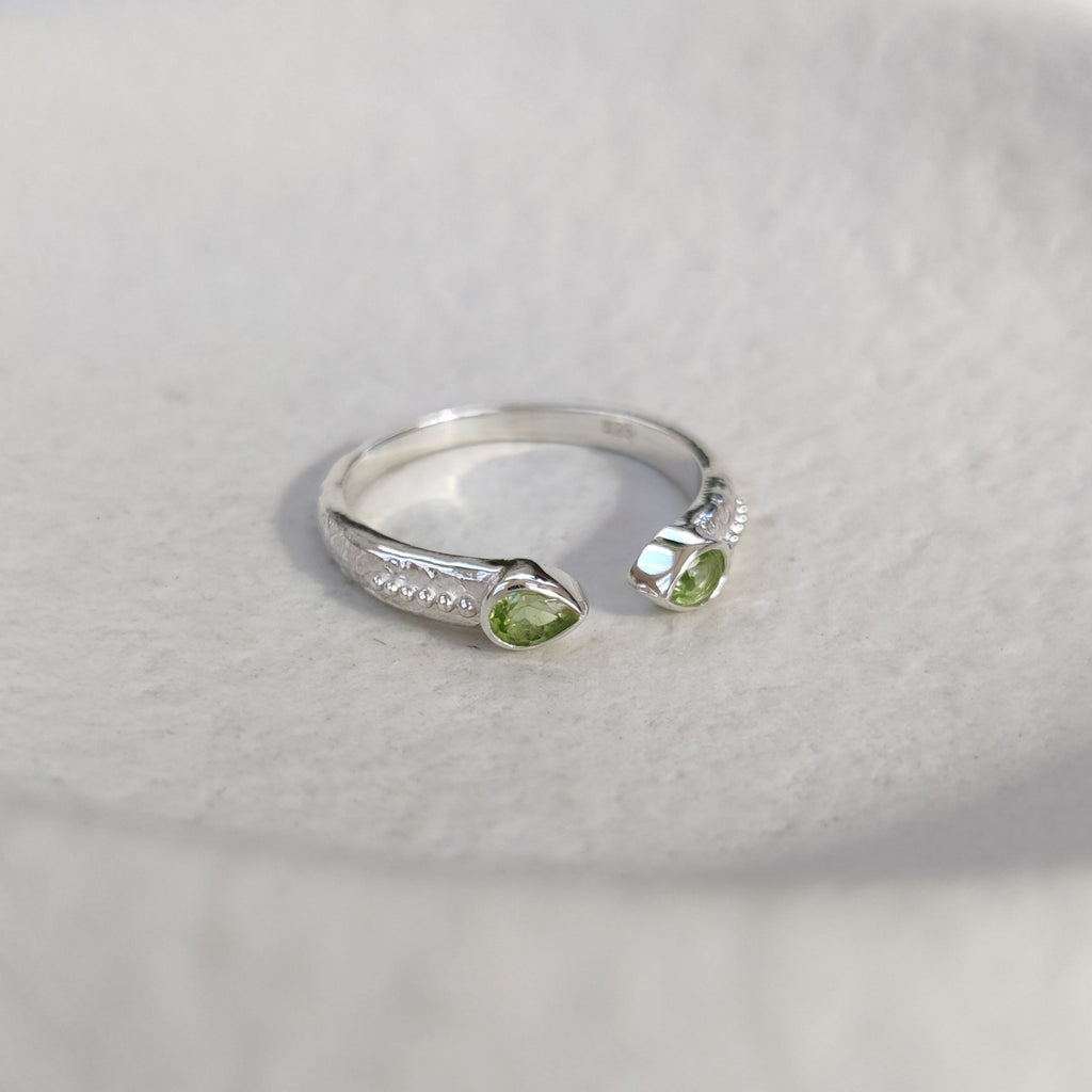 Open cuff silver ring with green gemstones on a white background