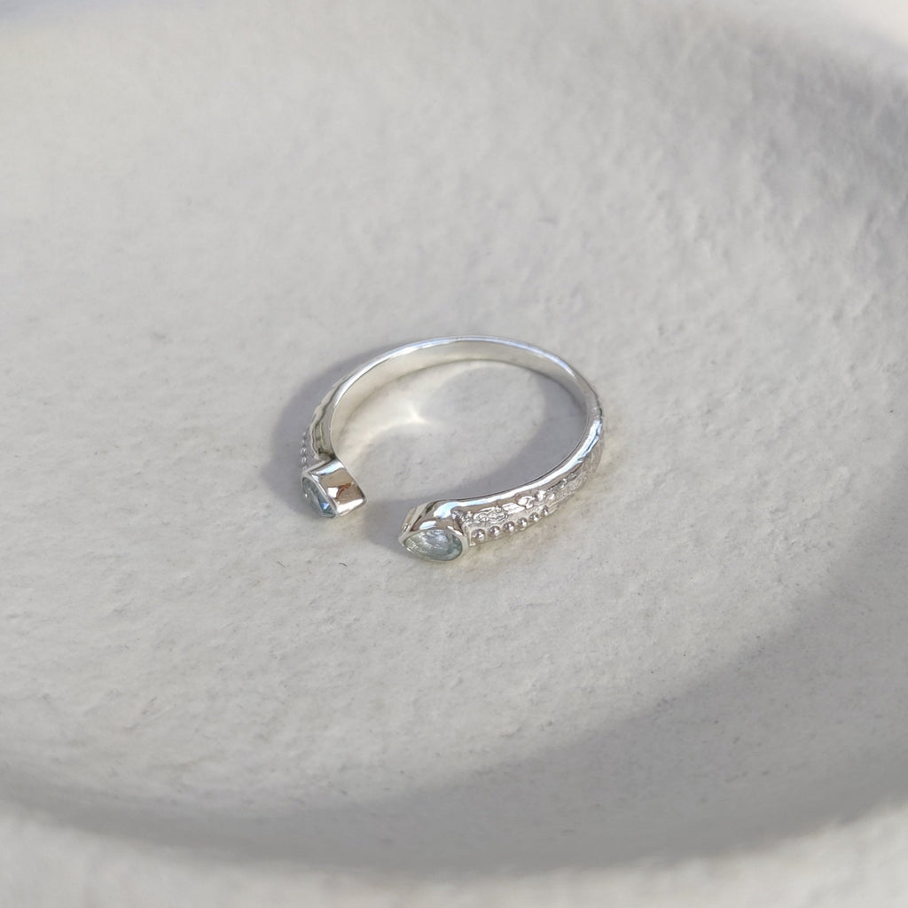Open cuff silver ring with small stones on a textured white surface