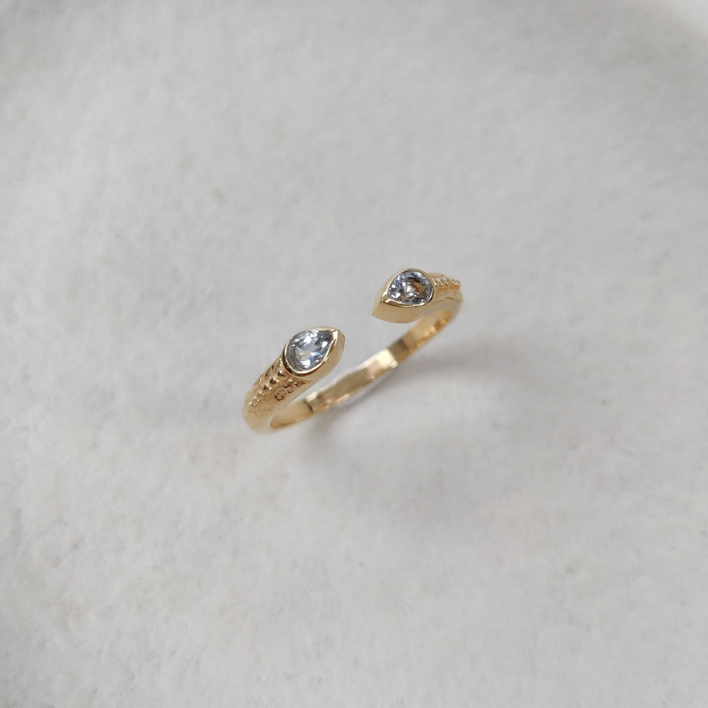 Gold ring with small blue topaz stones on a textured white surface.