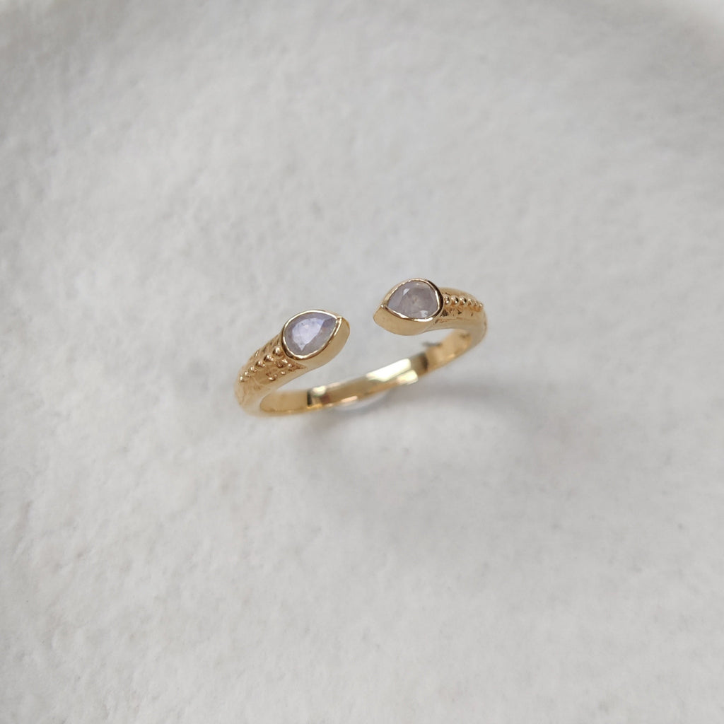 Open cuff ring in gold with moonstones on a white textured surface.