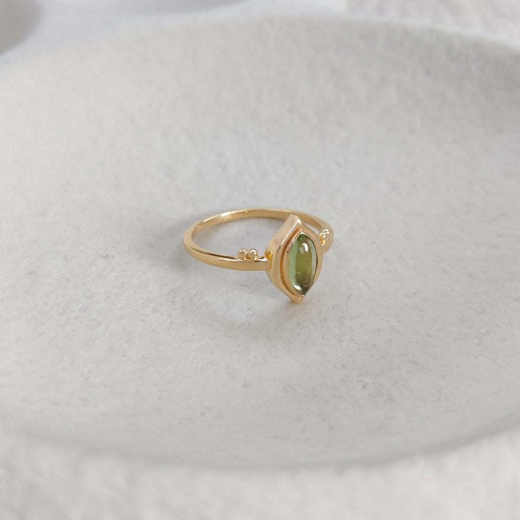 Gold ring with a green gemstone on a textured white surface.